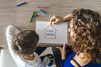 Two people drawing a house with the words Stay Home inside. 